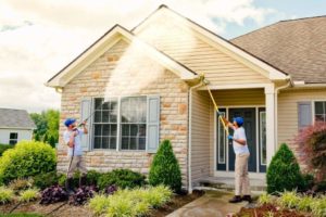 A man using a pressure washer to clean the exterior of a house.