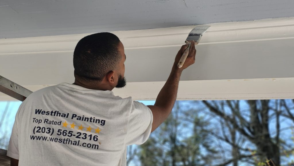 A meticulous interior painter from Westfhal Painting and Drywall LLC cutting in a wall with a brush, wearing a Westfhal shirt
